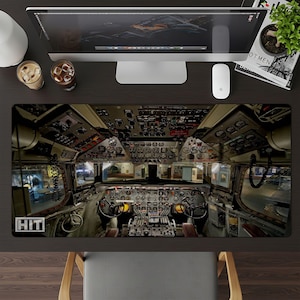 May include: A rectangular desk mat featuring a detailed image of an airplane cockpit interior. The mat has a dark background with various gauges, dials, and control panels. The word "HIT" is visible in the lower left corner.