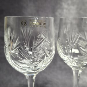 May include: Two clear crystal wine glasses with intricate etched designs. The glasses feature a starburst and leaf pattern. The text "S. Wiercie" is visible on the front of the glass. The stemware is elegant and suitable for special occasions.