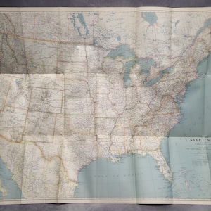 Peut inclure: Une carte pliée vintage des États-Unis, avec des informations géographiques détaillées. La carte est imprimée sur du papier vieilli avec une bordure et du texte bleu clair. Le titre "United States" est visible.