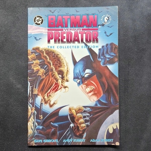 May include: A Batman Versus Predator The Collected Edition comic book featuring a cover illustration of Batman and the Predator facing each other. The title is printed in bold pink and blue letters at the top, with DC and Dark Horse Comics logos.