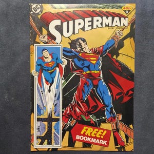 Peut inclure: Une bande dessinée Superman numéro 9 avec un fond jaune. La couverture montre Superman dans son costume bleu et rouge avec une cape rouge, volant au-dessus d'une ville. Le texte indique SUPERMAN, EVERY FORTNIGHT et FREE! BOOKMARK.