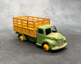 May include: A vintage die-cast toy truck featuring a green cab and a yellow slatted cargo bed. The metal vehicle shows signs of wear with chipped paint on the hood and sides. It has small yellow wheels and a front grille with two round headlights.