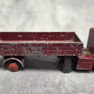 Peut inclure: Un camion jouet vintage bordeaux avec une plate-forme. Le camion présente des signes d'usure, avec de la peinture écaillée. Les roues sont noires et rouges. La cabine est arrondie. Un jouet de collection classique.
