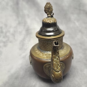 Peut inclure: Une théière antique avec un corps marron, des accents en laiton et un couvercle décoratif. Le bec et la poignée sont finement conçus avec des détails ornés. La théière a une esthétique vintage, suggérant qu'il s'agit d'un objet de collection.