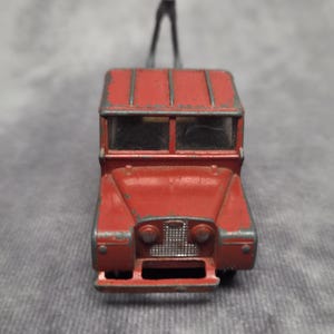 Puede incluir: Un camión de remolque de juguete rojo vintage con un brazo de grúa negro. El camión de juguete tiene una parrilla delantera detallada, faros y ventanas. La pintura muestra signos de desgaste, dándole un aspecto clásico y antiguo.