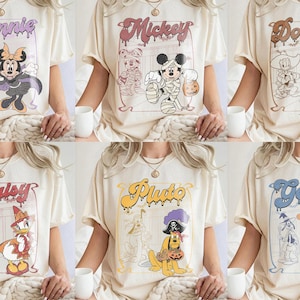 May include: A collection of six cream-colored t-shirts, each featuring a different Disney character in a Halloween costume. The designs include Minnie as a vampire, Mickey as a mummy, Donald as a cowboy, Daisy as a witch, Pluto as a pirate, and Goofy as a wizard, all with their names in a dripping font.