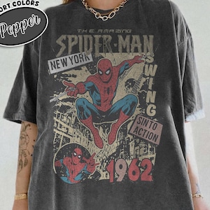 May include: Dark gray t-shirt featuring a vintage Spider-Man graphic. The design includes the text "THE AMAZING SPIDER-MAN", "NEW YORK", and "1962". The shirt has a distressed look and a round neckline.