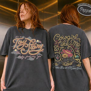 K&ouml;nnte beinhalten: Ein anthrazitfarbenes T-Shirt mit einem Frontaufdruck mit dem Text Toy Story und einem R&uuml;ckenaufdruck mit dem Text Cowgirl like me, Takes One to Know One, sowie Comfort Colors Pepper. Die Designs zeigen Seil-Schriftz&uuml;ge und einen Hut.