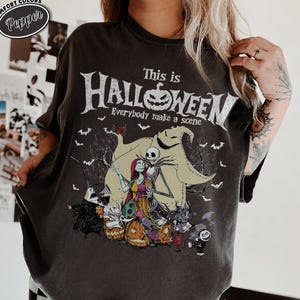 May include: Dark gray t-shirt featuring a graphic from "The Nightmare Before Christmas." The design includes Jack Skellington, Sally, and Oogie Boogie, with the text "This is Halloween" and "Everybody make a scene."