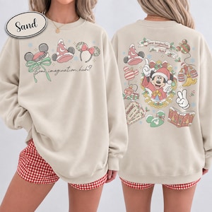Peut inclure: Un sweat-shirt à col rond couleur sable avec une impression graphique. Le devant présente trois icônes et le texte "Some imagination, huh?". Le dos montre une grande illustration d'un personnage avec un bonnet de Noël, entouré d'icônes festives.