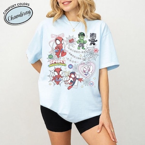 以下が含まれることがあります： スパイダーマンなどのキャラクターの漫画イラストが描かれた水色のTシャツ。「Spidey and Amazing Friends」と「Comfort Colors Chambray」の文字が円形にデザインされています。