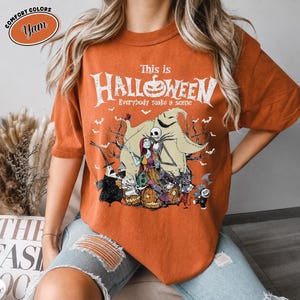 Puede incluir: Camiseta naranja con un dise&ntilde;o de "Pesadilla antes de Navidad". El dise&ntilde;o presenta a Jack Skellington, Sally y otros personajes, con el texto "This is Halloween". La camiseta tiene mangas cortas y cuello redondo.