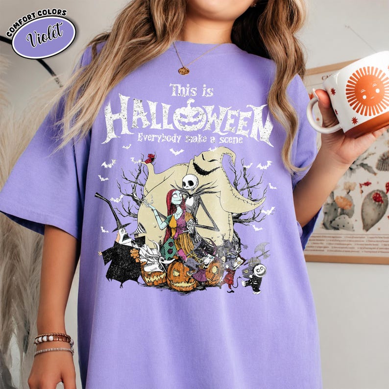 Puede incluir: Una camiseta violeta con un dise&ntilde;o gr&aacute;fico de "Pesadilla antes de Navidad". El dise&ntilde;o presenta a Jack Skellington, Sally y otros personajes, con el texto "This is Halloween" y "Everybody make a scene."