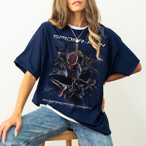 May include: Navy blue Spider-Man graphic t-shirt. The shirt features a large graphic of Spider-Man and other characters from the movie. The text "SPIDER-MAN" is printed across the top, and the phrase "WITH GREAT POWER COMES GREAT RESPONSIBILITY" is printed at the bottom.