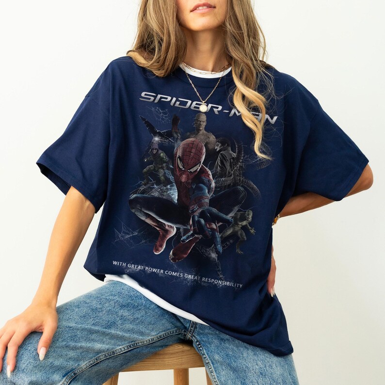May include: Navy blue Spider-Man graphic t-shirt. The shirt features a large graphic of Spider-Man and other characters from the movie. The text "SPIDER-MAN" is printed across the top, and the phrase "WITH GREAT POWER COMES GREAT RESPONSIBILITY" is printed at the bottom.