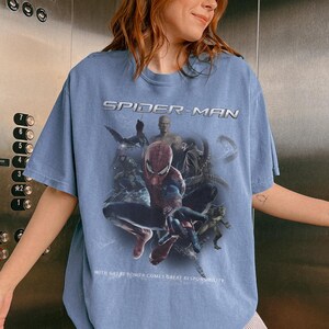 May include: Pale blue Spider-Man t-shirt with a graphic of Spider-Man and other characters. The text "SPIDER-MAN" is across the top, and "WITH GREAT POWER COMES GREAT RESPONSIBILITY" is at the bottom.