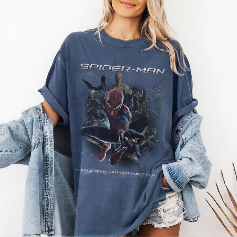 May include: A navy blue Spider-Man t-shirt with a graphic of Spider-Man and other characters. The text "SPIDER-MAN" is printed across the top, with the phrase "WITH GREAT POWER COMES GREAT RESPONSIBILITY" at the bottom.