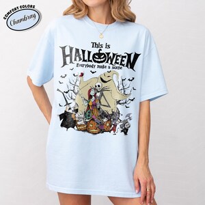 Puede incluir: Camiseta azul claro con un dise&ntilde;o de "Pesadilla antes de Navidad". El dise&ntilde;o incluye el texto "This is Halloween" con Jack Skellington, Sally y otros personajes. La camiseta es de la marca Comfort Colors.