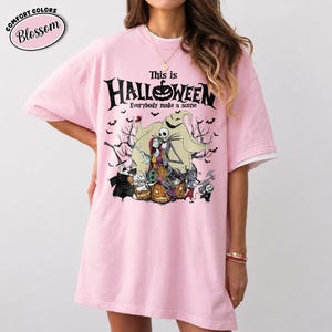 Puede incluir: Una camiseta rosa claro con un gr&aacute;fico de "Pesadilla antes de Navidad". El dise&ntilde;o presenta a Jack Skellington, Sally y otros personajes con el texto "This is Halloween" y "Everybody make a scene". La camiseta tiene mangas blancas.