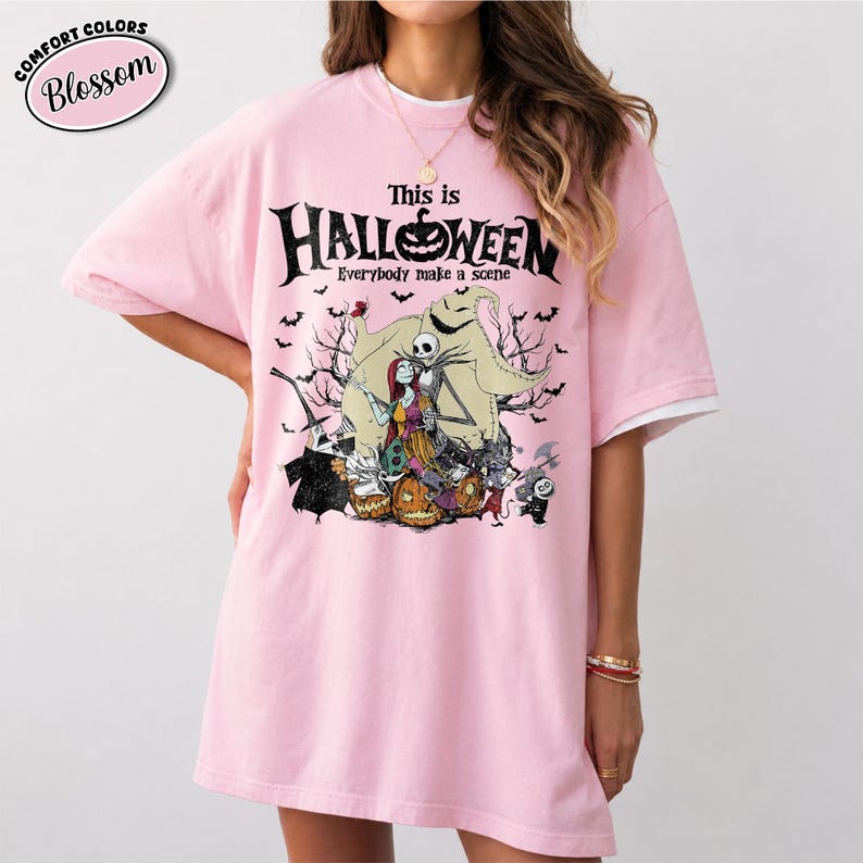 Puede incluir: Una camiseta rosa claro con un gr&aacute;fico de "Pesadilla antes de Navidad". El dise&ntilde;o presenta a Jack Skellington, Sally y otros personajes con el texto "This is Halloween" y "Everybody make a scene". La camiseta tiene mangas blancas.