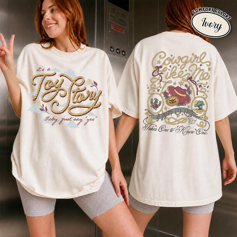 K&ouml;nnte beinhalten: Ein elfenbeinfarbenes T-Shirt mit einer Vorderseite, die den seilartigen Schriftzug "it's a Toy Story" und "Baby, just say yes" zeigt. Die R&uuml;ckseite zeigt ein Lasso-Design, einen Cowboyhut sowie den Text "Cowgirl like Me" und "Takes One to Know One".