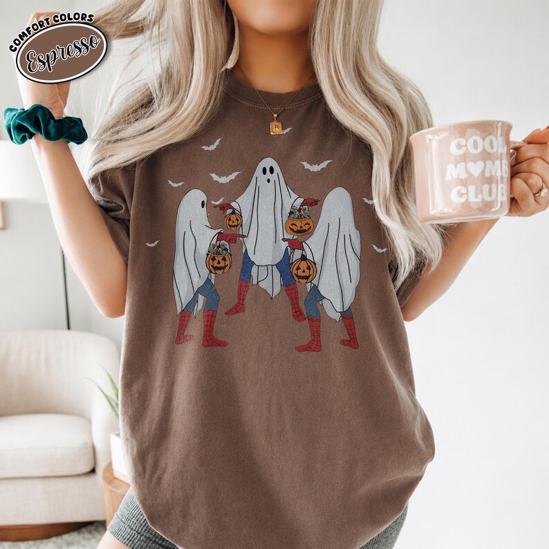 May include: Espresso-coloured t-shirt with a Halloween graphic. The design shows three ghosts holding jack-o'-lanterns, with bat silhouettes above. The shirt has a relaxed fit and is made of a soft material.