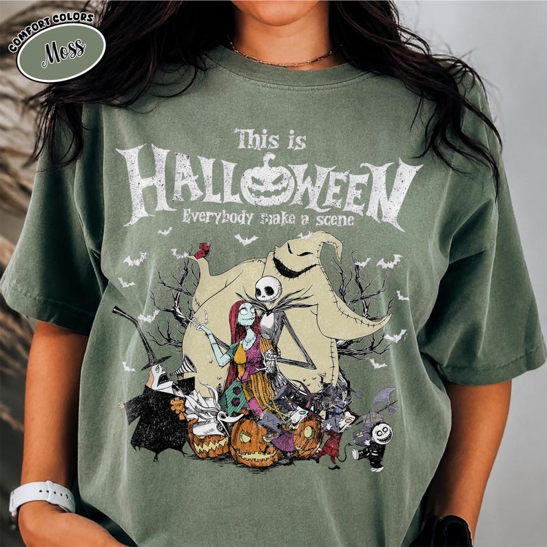 Puede incluir: Camiseta verde musgo con un gr&aacute;fico de "Pesadilla antes de Navidad". El dise&ntilde;o incluye a Jack Skellington, Sally, Oogie Boogie y otros personajes, con el texto "This is Halloween" y "Everybody make a scene."