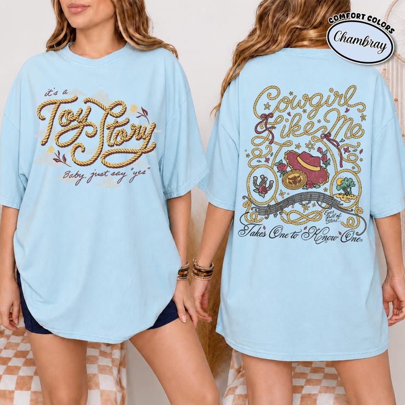 K&ouml;nnte beinhalten: Ein hellblaues T-Shirt mit einer Vorderseite, die den seilartigen Schriftzug "it's a Toy Story Baby, just say 'yes'" zeigt, und einer R&uuml;ckseite mit Seilbord&uuml;ren, einem Cowboyhut, einem Hufeisen und dem Text "Cowgirl like Me Takes One to Know One."