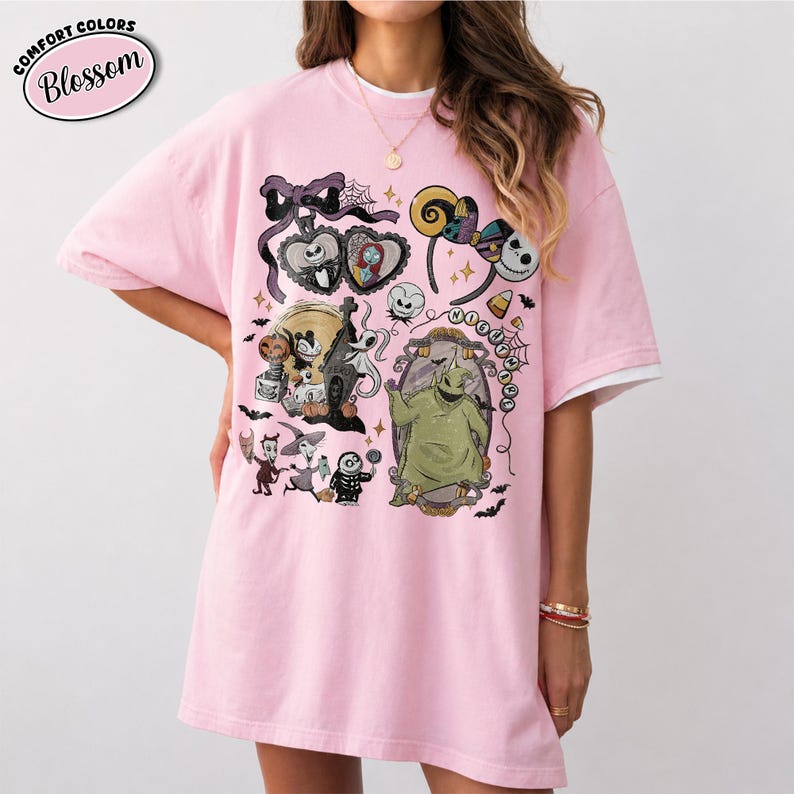 May include: A light pink short-sleeved t-shirt featuring a graphic print of characters from The Nightmare Before Christmas, including Jack Skellington, Sally, and Oogie Boogie, along with a spiderweb, bats, and a headband with ears.