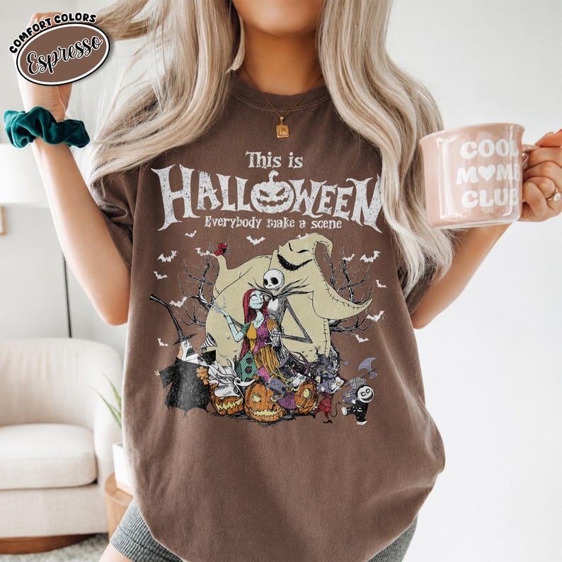 Puede incluir: Camiseta color espresso con un dise&ntilde;o tem&aacute;tico de Halloween. El dise&ntilde;o incluye el texto "This is Halloween" con una calabaza y varios personajes. La camiseta es de la marca Comfort Colors.