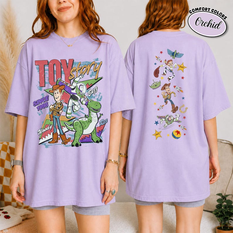 K&ouml;nnte beinhalten: Ein orchideenfarbenes T-Shirt mit Toy Story-Grafiken. Die Vorderseite zeigt Woody, Buzz Lightyear und Rex mit dem Text "TOY story SINCE 1995". Die R&uuml;ckseite zeigt eine vertikale Anordnung von Charakteren, darunter Woody, Buzz und ein Alien mit Sternen.