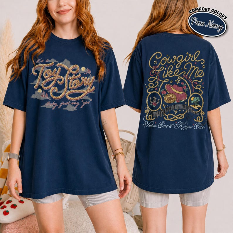 K&ouml;nnte beinhalten: Ein marineblaues T-Shirt mit einer seilartigen Grafik auf der Vorderseite mit der Aufschrift Toy Story und einer R&uuml;ckengrafik mit dem Text Cowgirl Like Me, Takes One to Know One, umgeben von Illustrationen eines Cowboyhuts, eines Seils und einer W&uuml;stenlandschaft.