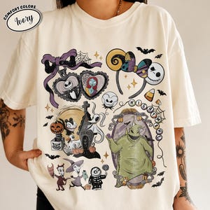 May include: An ivory t-shirt featuring a graphic print of characters from The Nightmare Before Christmas, including Jack Skellington, Sally, Zero, and Oogie Boogie, alongside icons like a heart locket, mouse ears, and bats, with the text "NIGHTMARE".