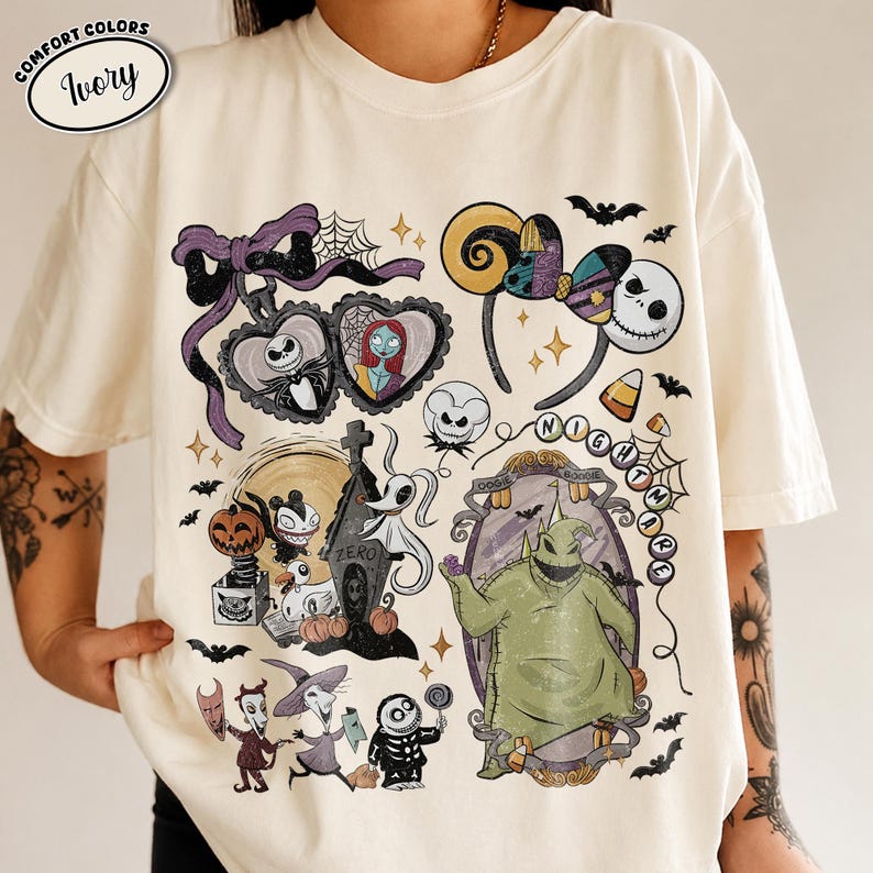 May include: An ivory t-shirt featuring a graphic print of characters from The Nightmare Before Christmas, including Jack Skellington, Sally, Zero, and Oogie Boogie, alongside icons like a heart locket, mouse ears, and bats, with the text "NIGHTMARE".