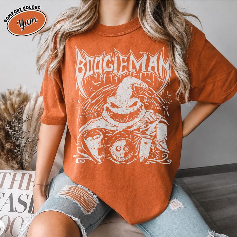 K&ouml;nnte beinhalten: Orangefarbenes T-Shirt mit einem wei&szlig;en Aufdruck der Figur Boogieman. Das Design zeigt das Wort "BOOGIEMAN" in einer stilisierten Schriftart &uuml;ber dem Gesicht der Figur. Das Shirt ist eine Komfortfarbe und hat kurze &Auml;rmel.