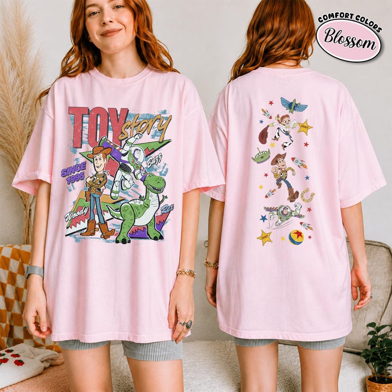 K&ouml;nnte beinhalten: Ein hellrosa T-Shirt mit Toy Story-Grafiken. Die Vorderseite zeigt Woody, Buzz Lightyear und Rex mit dem Text Toy Story Since 1995. Die R&uuml;ckseite zeigt eine vertikale Anordnung verschiedener Charaktere und Symbole, darunter Sterne und Raketen.