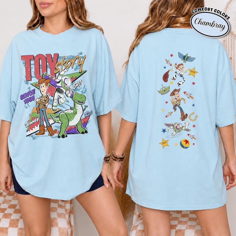 K&ouml;nnte beinhalten: Ein hellblaues T-Shirt mit Toy Story-Grafiken. Die Vorderseite zeigt Woody, Buzz Lightyear und Rex mit dem Text "TOY story SINCE 1995". Die R&uuml;ckseite zeigt eine vertikale Anordnung von Charakteren, darunter Woody, Buzz und ein Alien mit Sternen.