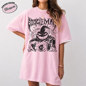 K&ouml;nnte beinhalten: Hellrosa T-Shirt mit einem schwarzen Aufdruck des Boogie Man aus The Nightmare Before Christmas. Der Aufdruck enth&auml;lt den Text "BOOGIEMAN" in einer gotischen Schriftart sowie andere Charakterbilder. Das Shirt hat ein wei&szlig;es Unterhemd, das aus den &Auml;rmeln herausschaut.