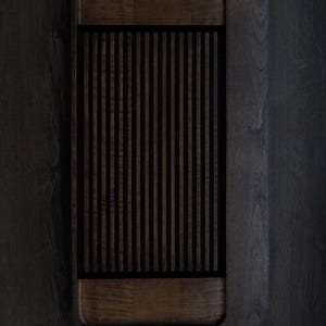 Op de afbeelding: Een rechthoekig houten dienblad met een donkerbruine afwerking. De lade heeft een gedeelte met verticale lamellen in het midden, omlijst door een donkerdere rand. Minimalistisch, modern ontwerp.
