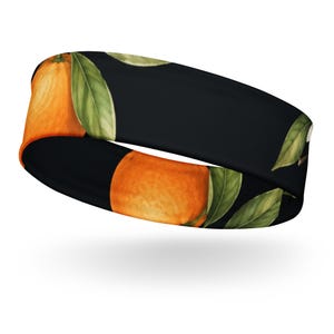 Könnte beinhalten: Ein schwarzes Stirnband mit einem sich wiederholenden Muster aus leuchtend orangefarbenen Zitrusfrüchten und länglichen grünen Blättern. Das Design zeigt mehrere ganze Orangen mit strukturierter Schale und detailliertem Blattwerk.
