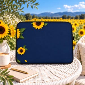Könnte beinhalten: Eine rechteckige Laptoptasche mit einem einfarbigen, dunkelblauen Hintergrund und einem Muster aus gelben Sonnenblumen mit grünen Blättern an der oberen und linken Kante. Die Tasche verfügt über einen schwarzen Reißverschluss an der Oberseite.