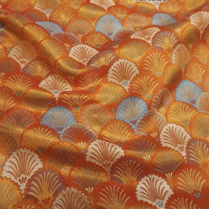 Puede incluir: Primer plano de una tela con un patrón repetido en forma de abanico. La tela presenta una paleta de colores cálidos de naranja, dorado y crema, con acentos de azul claro. El diseño es detallado y texturizado.