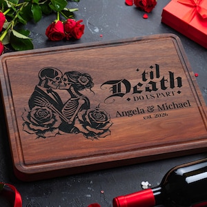 May include: A rectangular wooden cutting board with a dark brown finish. It features an engraved design of a skeleton couple kissing, surrounded by roses, with the text "'til Death Do Us Part" and personalized names and a year.