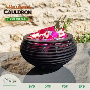 May include: A black, spherical, laser-cut cauldron bowl constructed from stacked horizontal rings. The bowl is filled with various colorful, individually wrapped candies. The text HALLOWEEN CAULDRON LASER CUT FILE is visible at the top left.