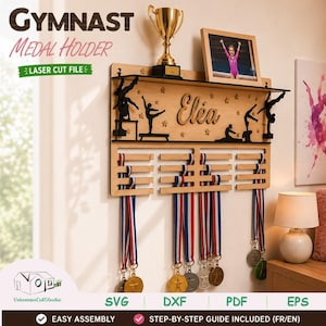 Peut inclure: Un porte-médailles mural en bois clair avec des silhouettes noires découpées de gymnastes, des étoiles et le prénom Eléa en écriture cursive. L'unité comprend une étagère supérieure avec un trophée doré et un cadre photo, ainsi que des barres horizontales pour suspendre des médailles avec des rubans rouge, blanc et bleu.