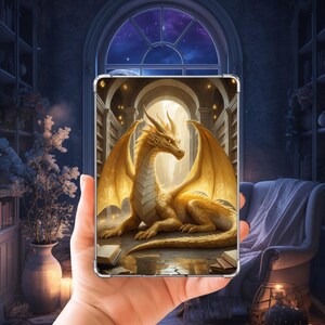Peut inclure: Une impression rectangulaire représentant un dragon doré aux grandes ailes posé sur un sol en pierre, entouré de livres ouverts. Le dragon est situé devant une arche lumineuse au sein d'une bibliothèque avec de hautes étagères.