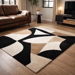 May include: A rectangular area rug with a geometric pattern in black, beige, and tan. The rug has an abstract design and is placed on a wooden floor. The rug is in a living room setting.