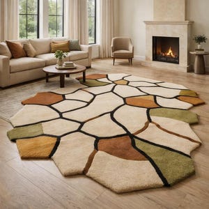 Könnte beinhalten: Ein großer, abstrakter Teppich mit einem einzigartigen geometrischen Design. Der Teppich hat eine cremefarbene Basis mit unregelmäßigen Formen in Braun-, Grün- und Goldtönen, die schwarz umrandet sind. Der Teppich befindet sich in einem Wohnzimmer.
