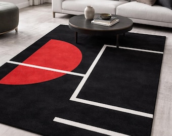 May include: Black rectangular area rug with a bold geometric design. A large red semi-circle and white lines create a modern pattern on the black background. The rug is placed in a living room setting.