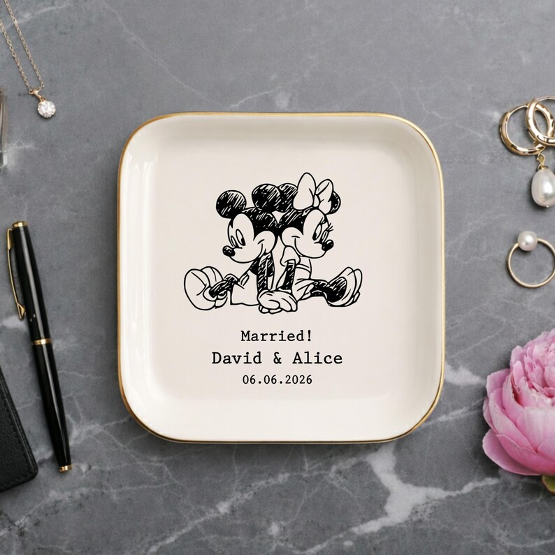 May include: A square white ceramic trinket dish with a gold-toned rim. The center features a black line-art illustration of two cartoon mice sitting back-to-back. Below the illustration, the text reads: Married! David & Alice 06.06.2026.